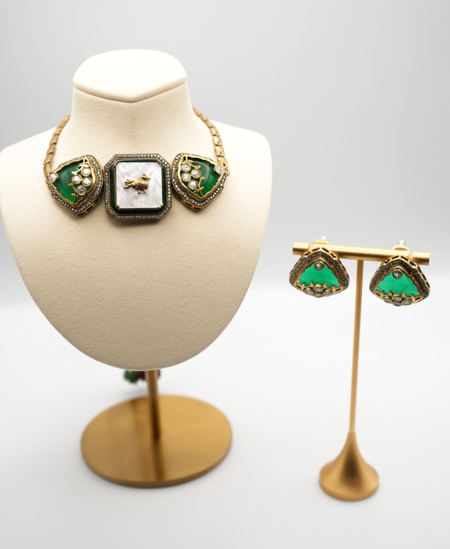 Gold- plated necklace with three gem-studded panels in deep green and white, accented by CZ stones and a bird motif.
